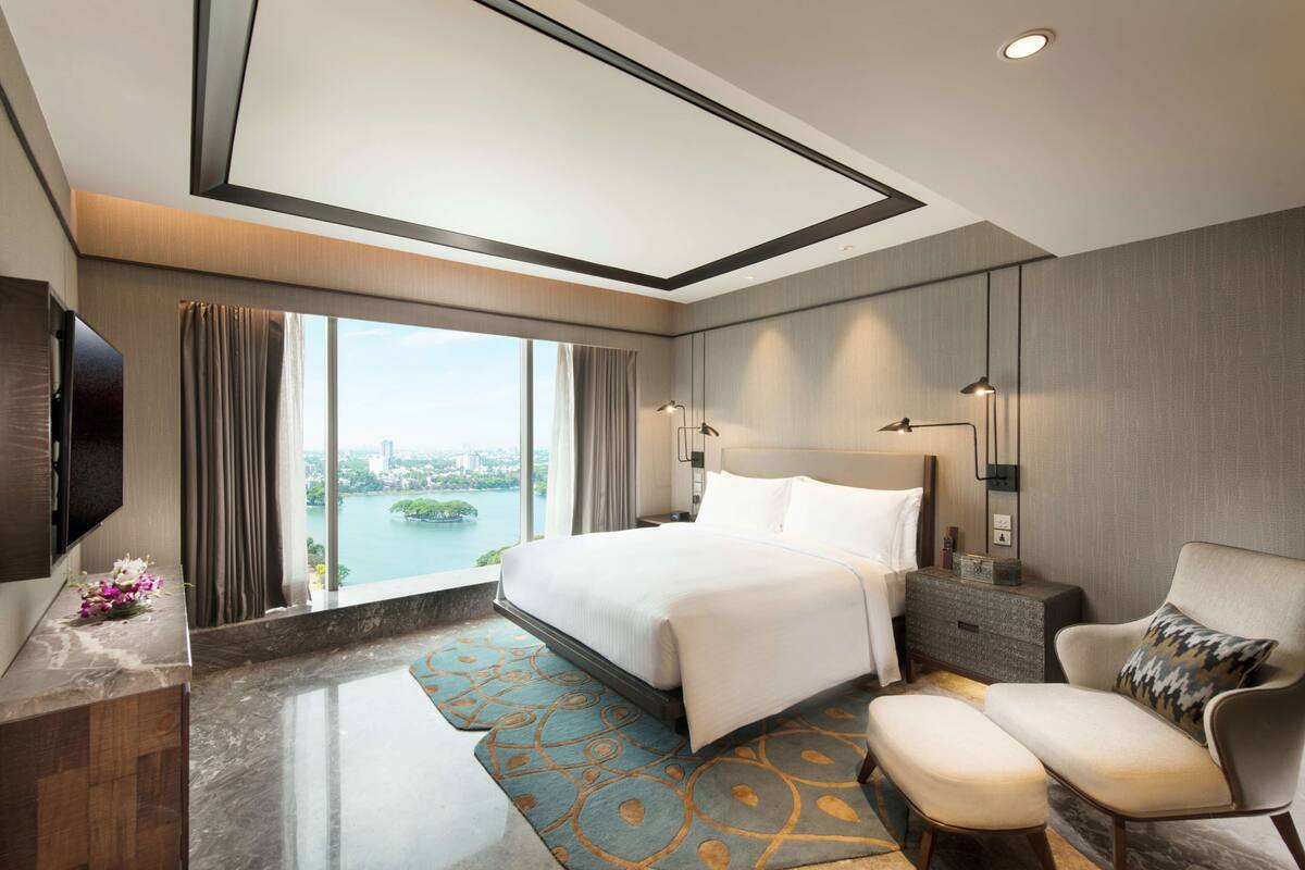 Una habitación de hotel moderna con una cama grande, una zona de estar, un televisor y vistas a un paisaje urbano.