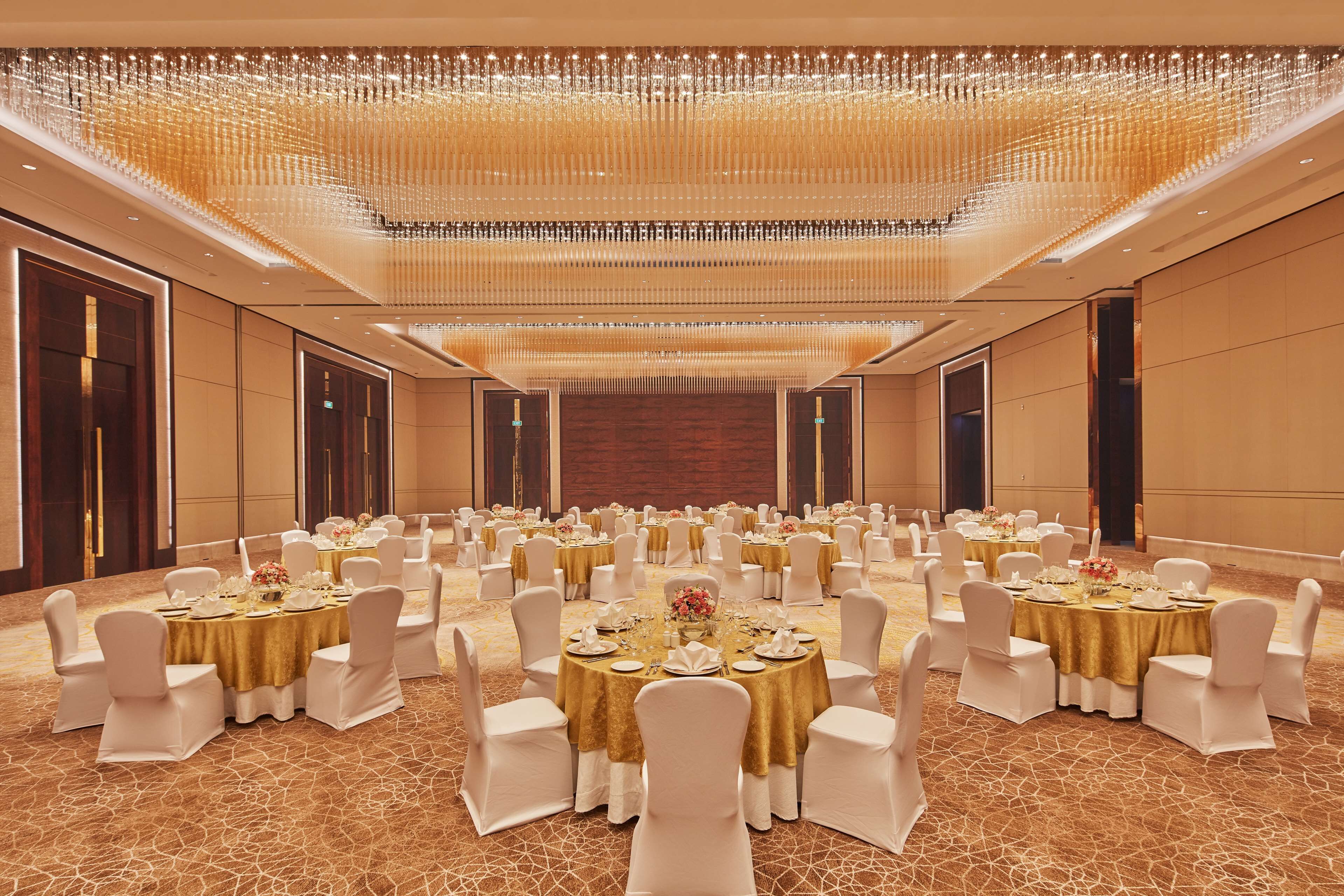 A banquet hall with multiple round tables, each set with white chairs and gold tablecloths, featuring a central floral arrangement.