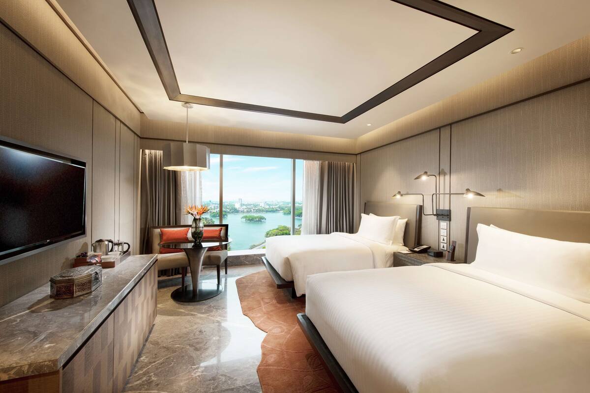 Una habitación de hotel moderna con una cama grande, un escritorio con televisor de pantalla plana, vistas a un cuerpo de agua y un paisaje urbano.