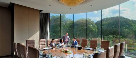 A conference room with a large oval table, leather chairs, and a chandelier.