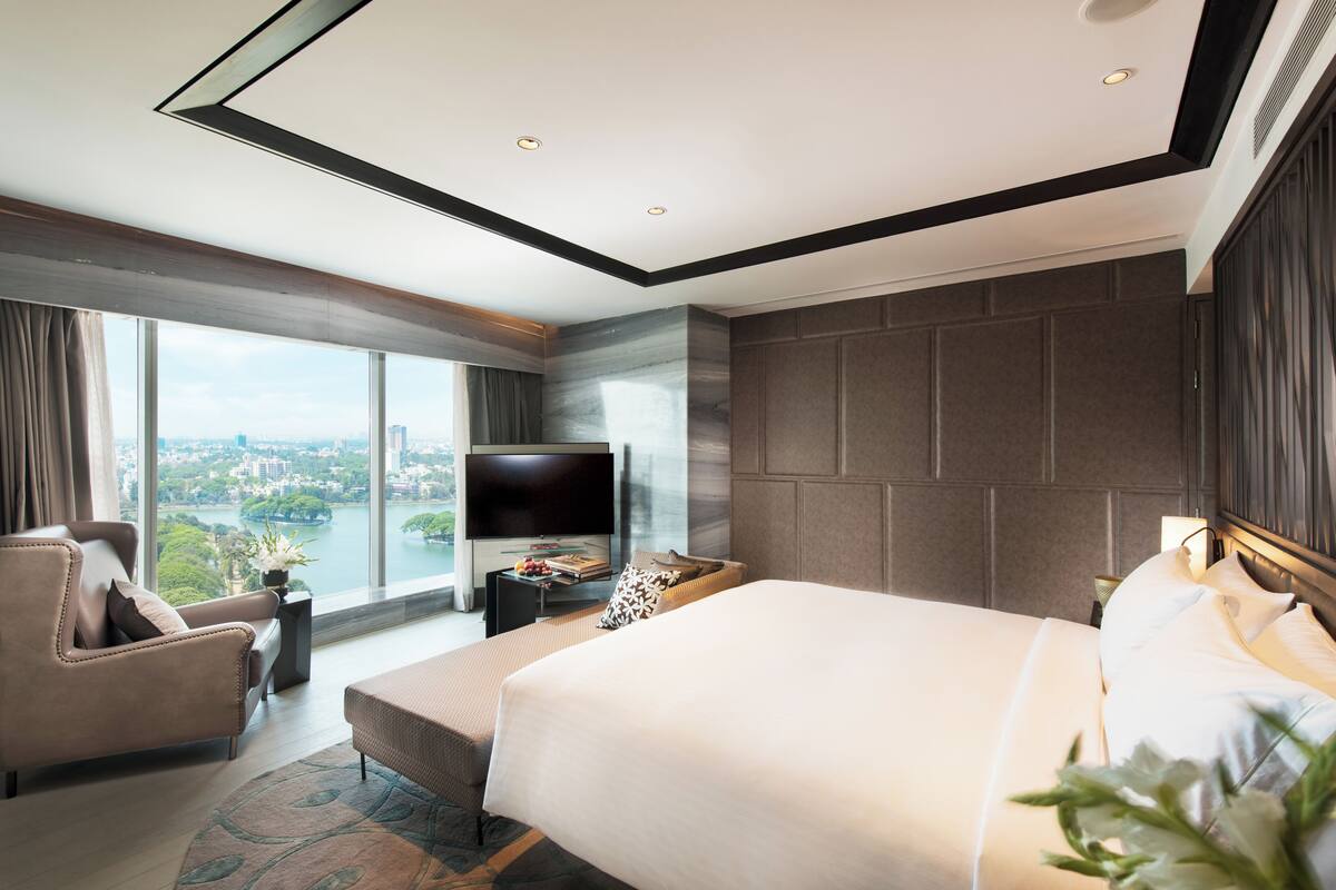 Una habitación de hotel moderna con una cama grande, un sofá, un televisor y vistas a un paisaje urbano.