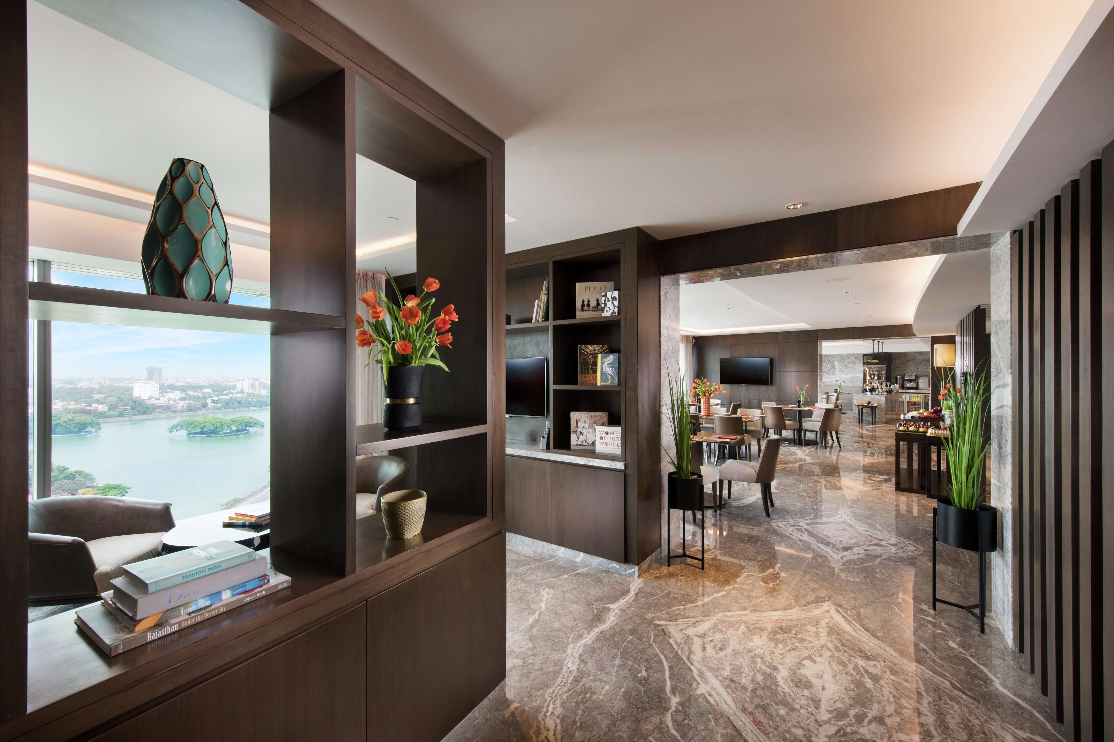 A modern interior with a view of a body of water, a dining area, and a living space with a TV and bookshelves.