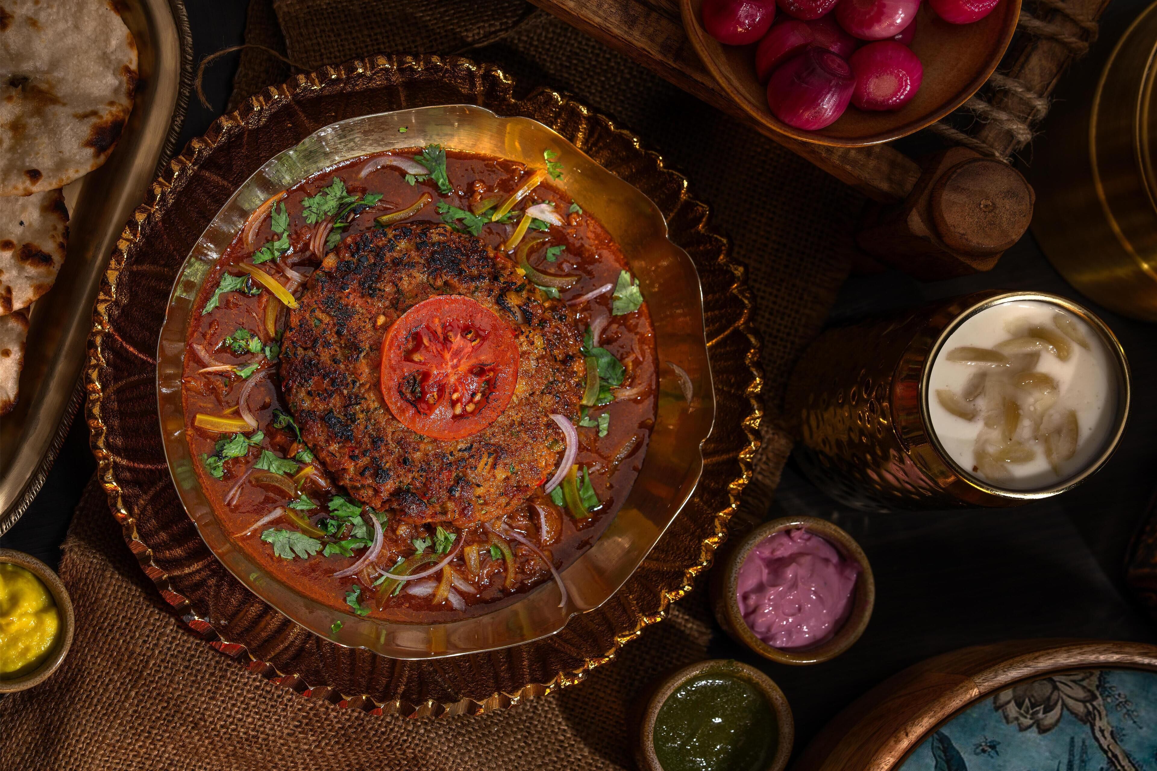 A traditional Indian meal with a variety of dishes, including a meat dish, flatbread, and several types of chutneys.