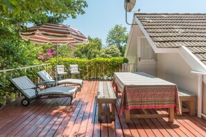 Um deck de madeira com cadeiras de descanso, uma mesa e um guarda-sol.