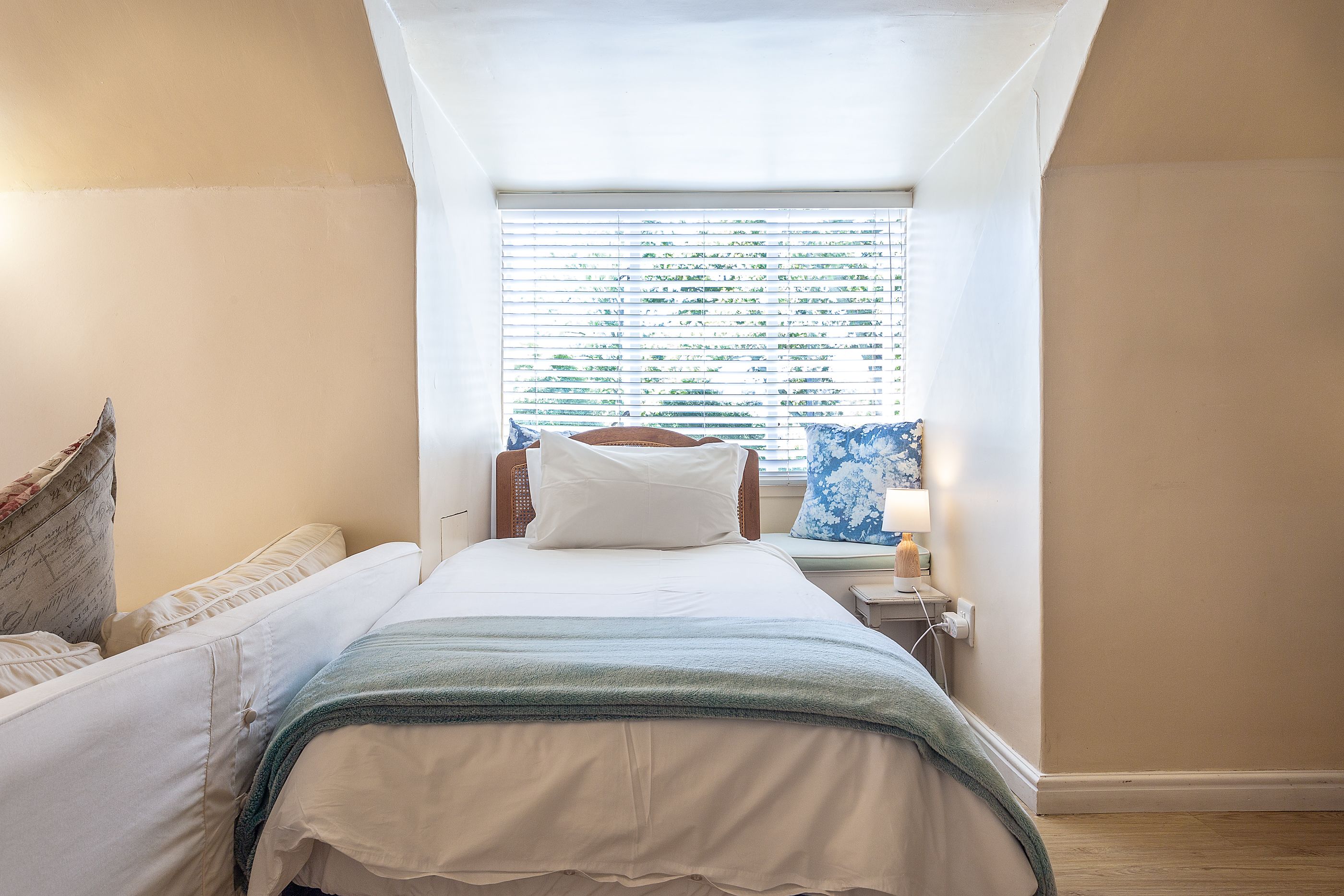 Un dormitorio pequeño y acogedor con una cama individual, una mesita de noche, una lámpara y una ventana con persianas.
