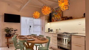 Una cocina moderna con comedor, que incluye una gran mesa de madera, sillas verdes, una estufa de acero inoxidable y un televisor de pantalla plana montado en la pared.