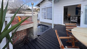Una terraza de madera con un jacuzzi, un muro de ladrillo y un edificio blanco con puerta de vidrio.