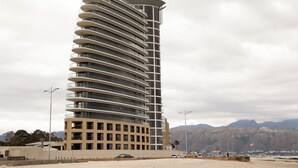 Un hotel moderno y alto, con fachada curva, varios balcones y vistas a montañas al fondo.