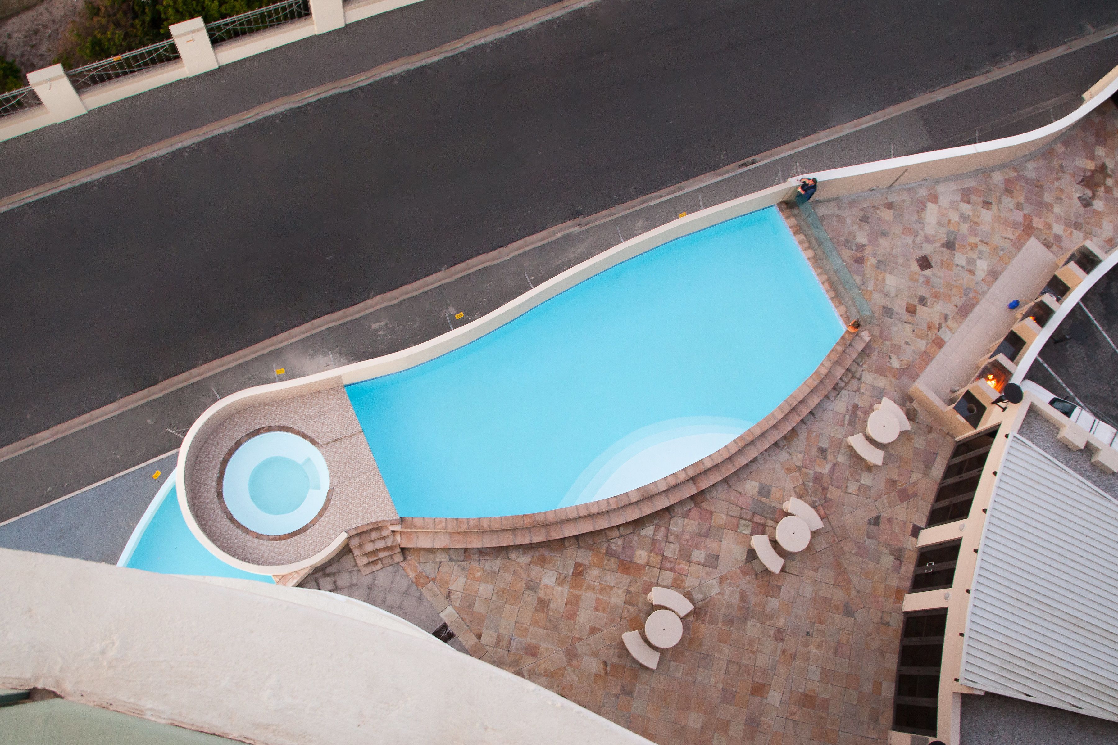 Una piscina con un área circular de hidromasaje, mobiliario exterior y un patio empedrado.