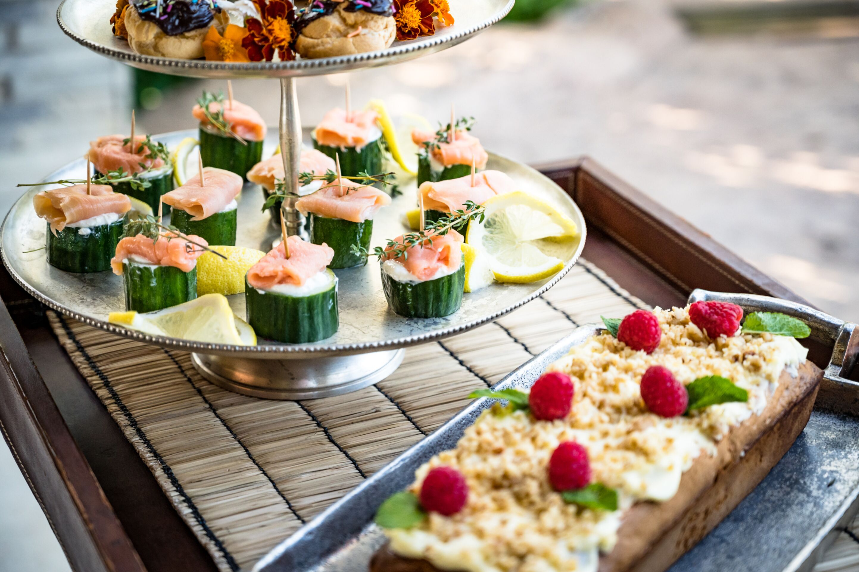 A tray with a variety of appetizers including smoked salmon on cucumber slices, lemon slices, and a dessert with raspberries.