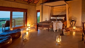 A spacious bedroom with a large bed, a balcony with a view, and several lanterns providing ambient lighting. - Makumu Private Game Lodge (Bushbuckridge)