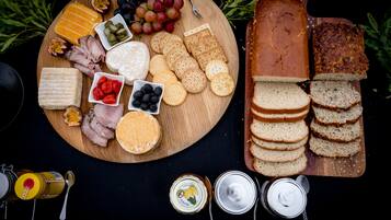 A wooden board with various cheeses, crackers, and sliced bread.
