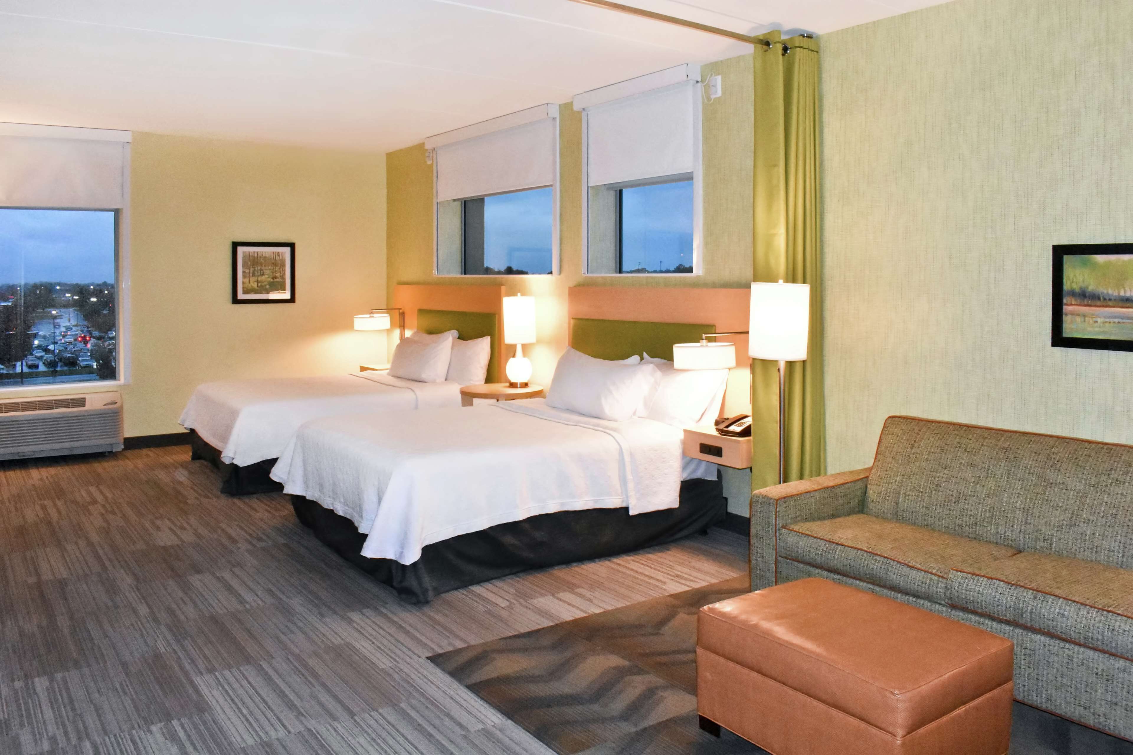 A hotel room with two beds, a sofa, and a view of the cityscape.
