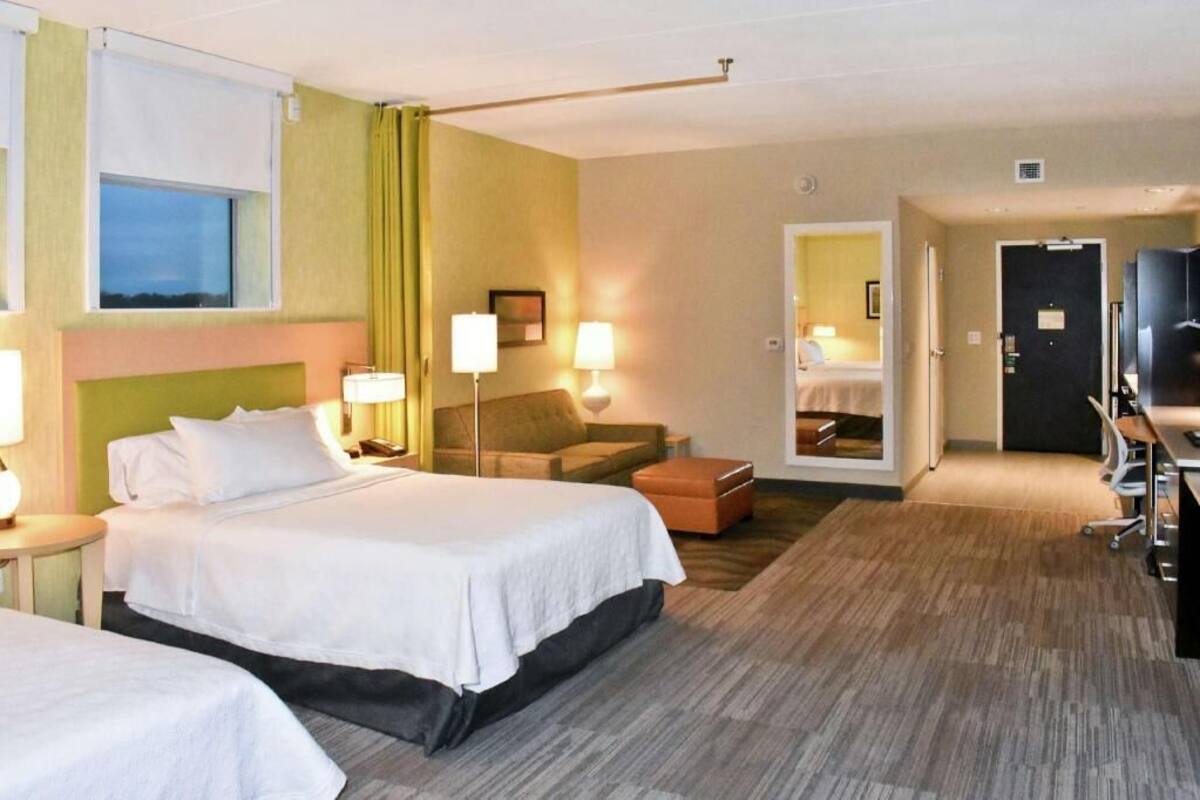 Habitación de hotel con dos camas, un sofá, un televisor y un espejo.