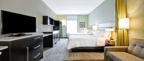 Una habitación de hotel con cama, escritorio con televisor, sofá y lámpara.