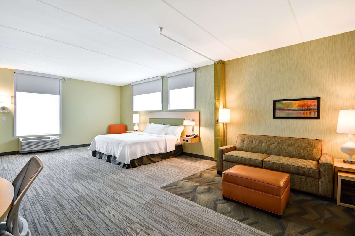 Une chambre d’hôtel avec un lit, un canapé, une chaise, une table et un tableau au mur.