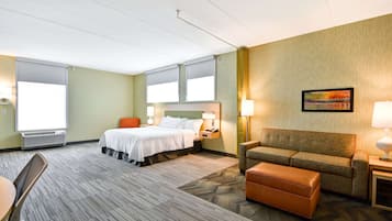 A hotel room with a bed, a sofa, a chair, a table, and a painting on the wall.