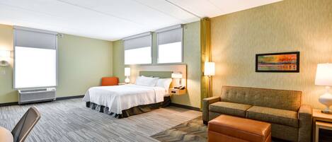 A hotel room with a bed, a sofa, a chair, a table, and a painting on the wall.