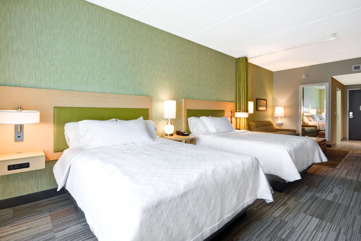 Une chambre d’hôtel avec deux lits, des tables de chevet avec des lampes, un miroir et une porte donnant sur une autre pièce.