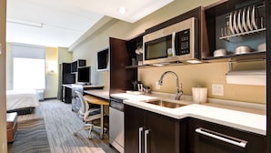 Une chambre d’hôtel moderne équipée d’une kitchenette, d’un lit, d’un bureau et d’une chaise.