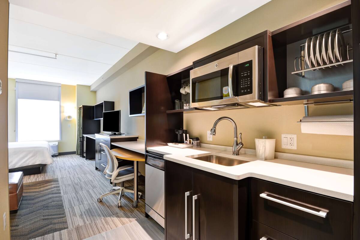 Une chambre d’hôtel moderne équipée d’une kitchenette, d’un lit, d’un bureau et d’une chaise.