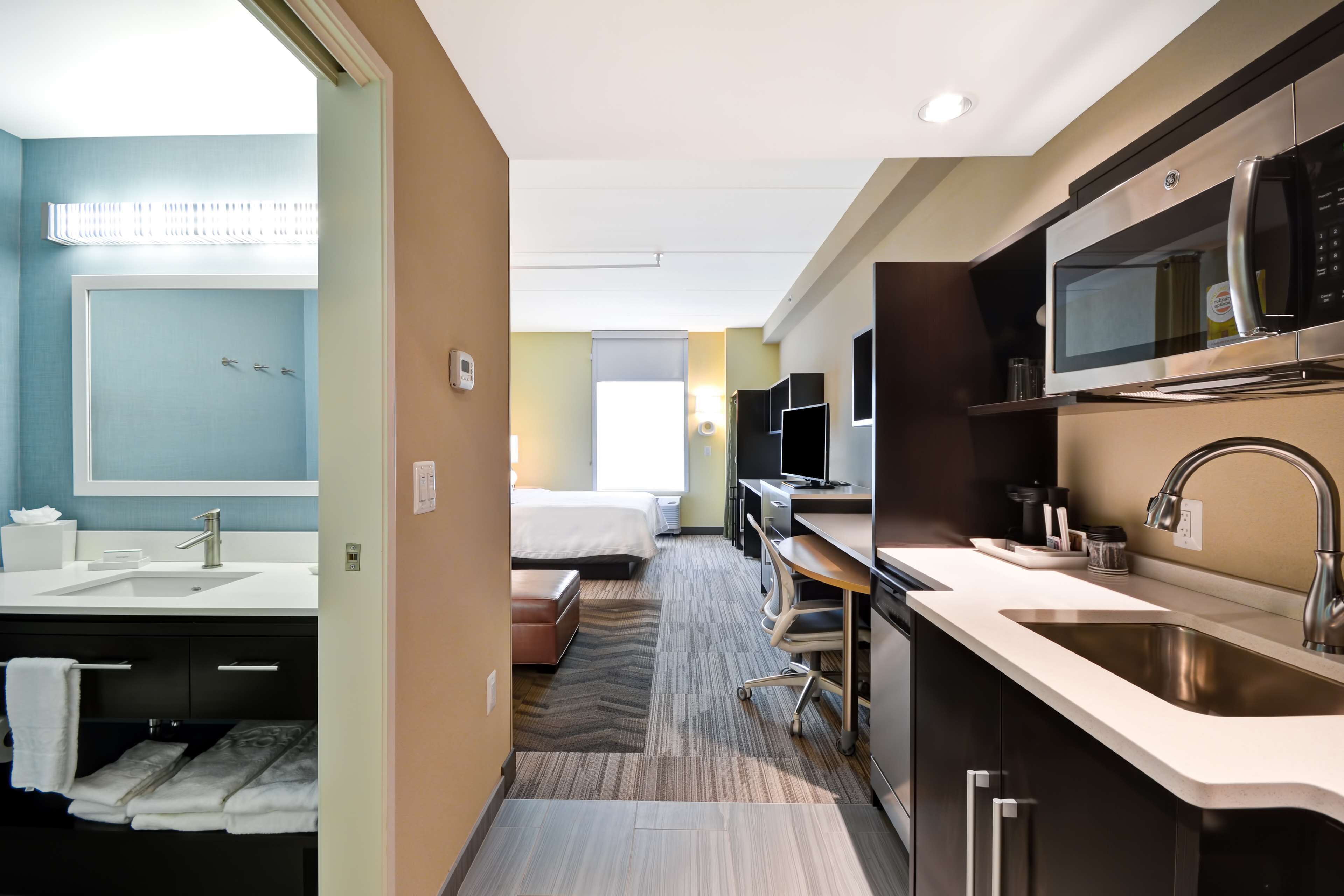 A modern hotel room with a large bed, a separate bathroom with a sink, a microwave, and a desk area.