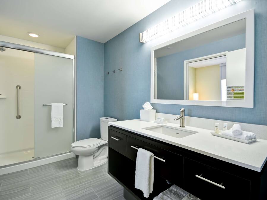 Et moderne badeværelse med en glasbrusekabine, et hvidt toilet, en vask med et spejl over og en sort kommode med skuffer.