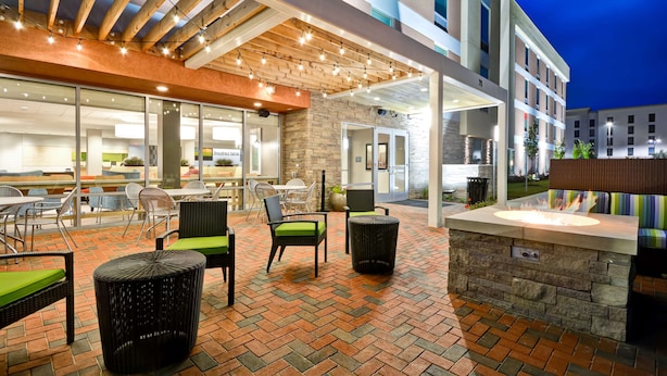 Un espace extérieur aménagé en terrasse, avec des meubles en osier, un foyer en pierre et un coin salon couvert agrémenté de guirlandes lumineuses.