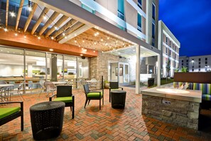 Un espace extérieur aménagé en terrasse, avec des meubles en osier, un foyer en pierre et un coin salon couvert agrémenté de guirlandes lumineuses.