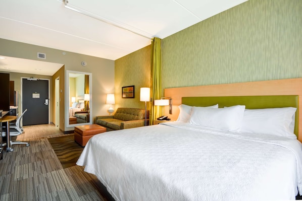 Ein Hotelzimmer mit einem großen Bett, einem Schreibtisch mit Stuhl, einem kleinen Tisch und einer Lampe.