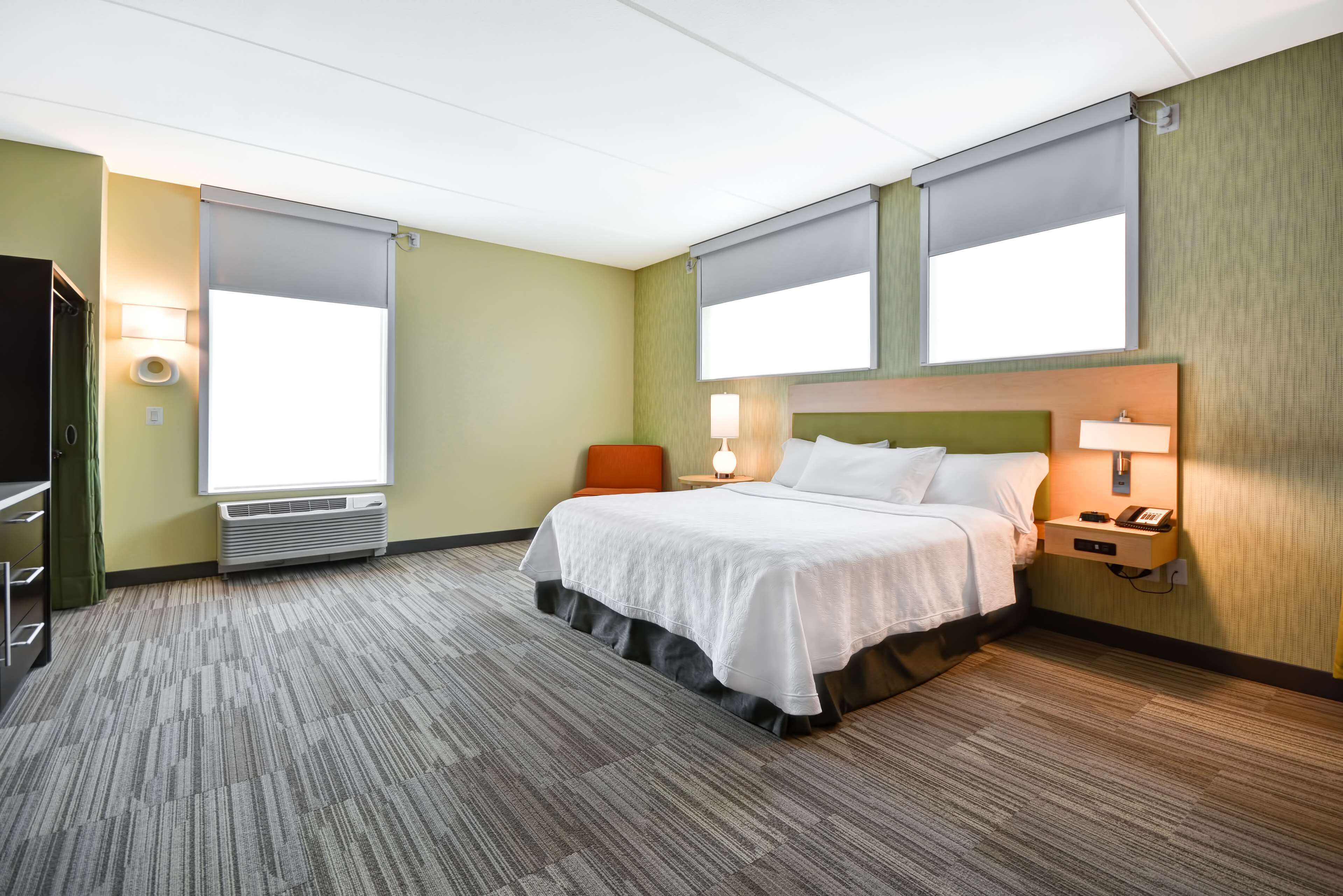 A hotel room with a bed, a chair, a desk, and a window.