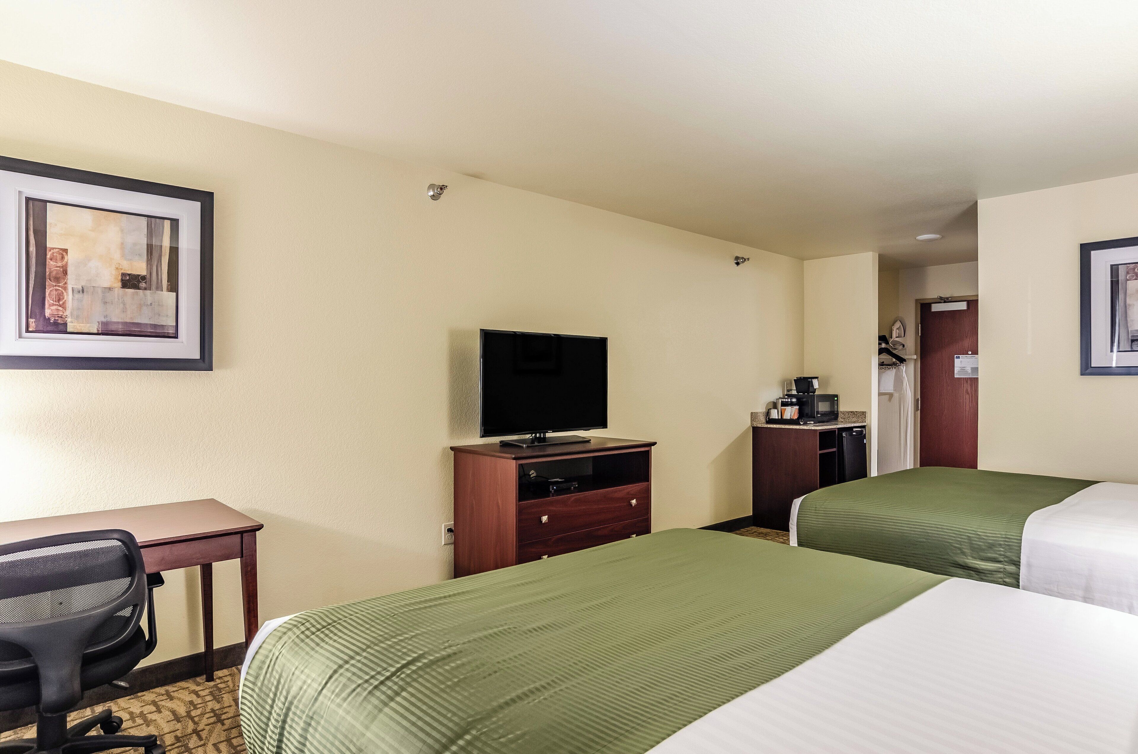 A hotel room with two beds, a desk with a chair, a television, and a coffee machine.