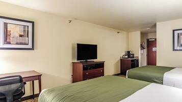A hotel room with two beds, a desk with a chair, a television, and a coffee machine.