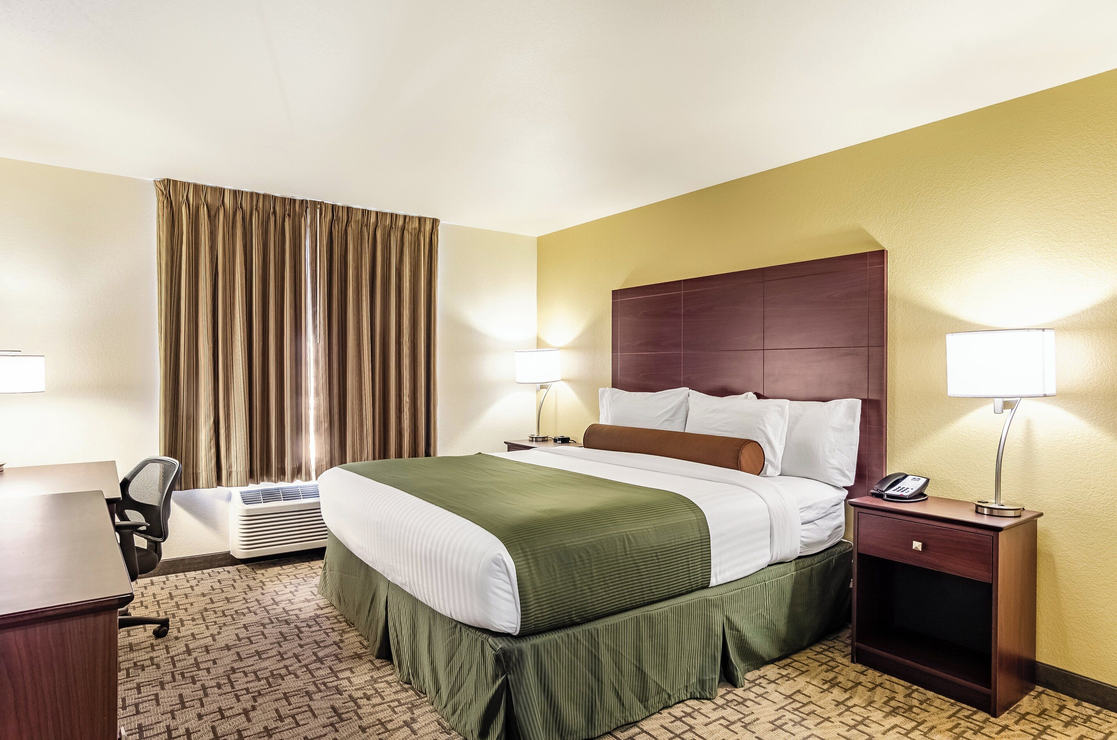 A hotel room with a bed, bedside lamps, a desk, and a chair.