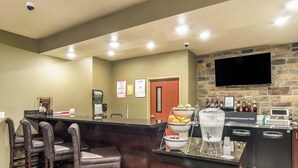 A bar area with a stone wall, a flat-screen TV, and a beverage dispenser. - Cobblestone Hotel & Suites - Gering/Scottsbluff (Gering)