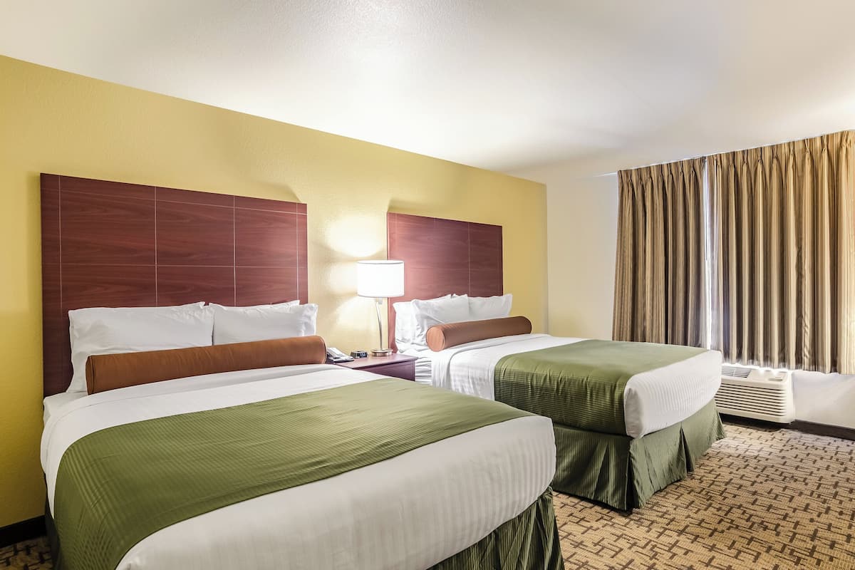 Habitació d'hotel amb dos llits, una tauleta de nit, una làmpada i una finestra amb cortines.