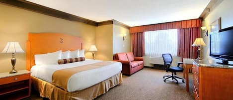 A hotel room with a large bed, a desk, a chair, a television, and a window with curtains.