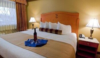 Habitación de hotel con una cama grande, dos mesitas de noche, una lámpara en cada una y un ventanal con cortinas.
