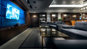 Ein modernes Wohnzimmer mit großem Flachbildfernseher, einer Couch, einem Couchtisch und einer Bar mit Pflanze und Barhocker.