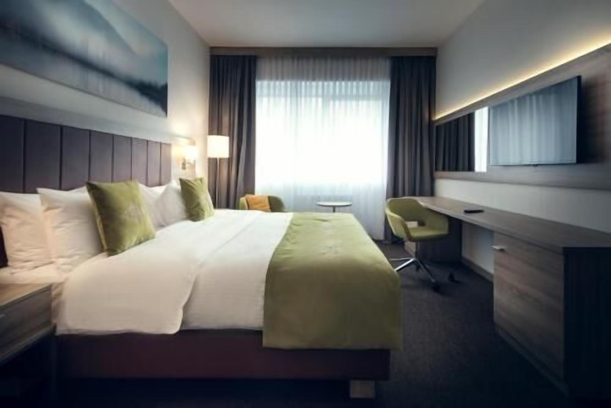 Une chambre d’hôtel équipée d’un lit, d’un bureau, d’une chaise, d’une télévision et d’une fenêtre avec des rideaux.