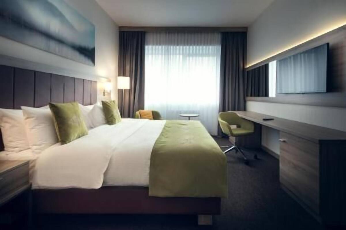 Une chambre d’hôtel équipée d’un lit, d’un bureau, d’une chaise, d’une télévision et d’une fenêtre avec des rideaux.