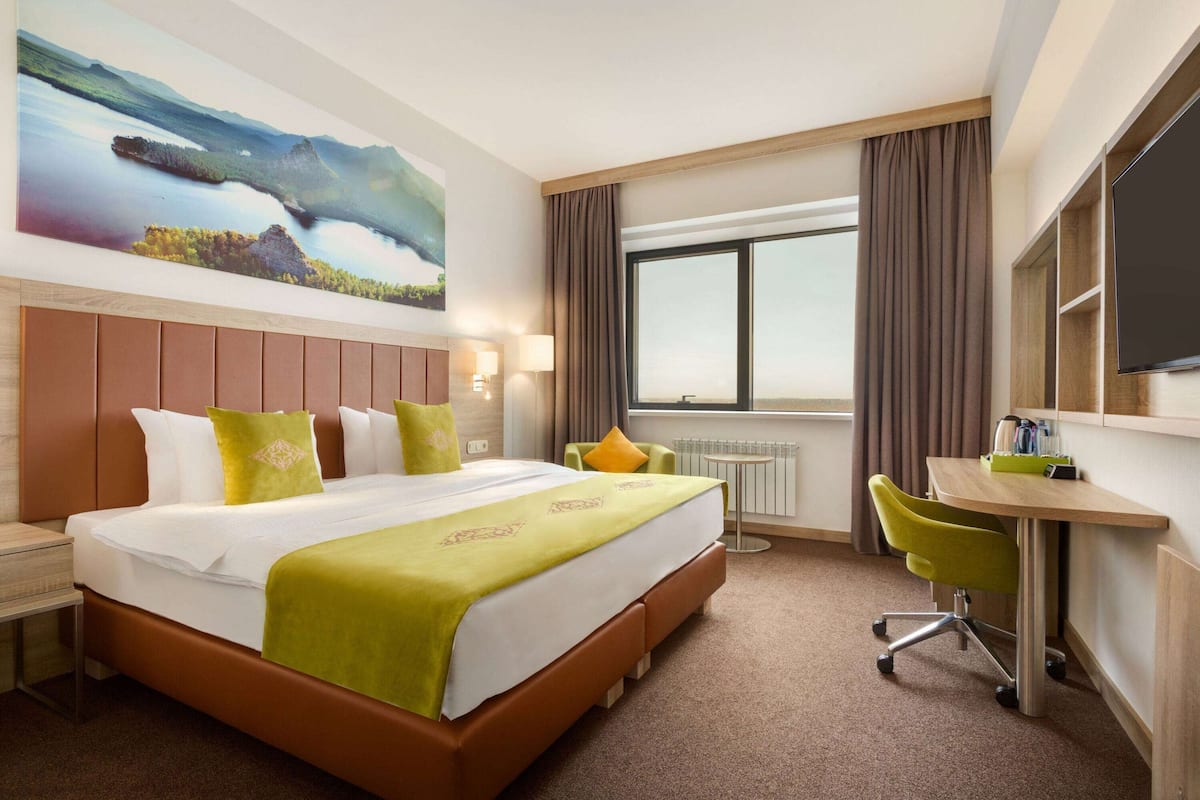 Habitación de hotel con una cama grande, un escritorio, una silla, un televisor y una ventana con cortinas.
