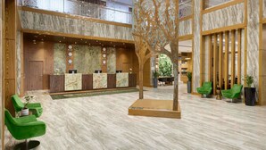 Eine Lobby mit einer Rezeption, grünen Sesseln, einer dekorativen Baumstruktur und einem Marmorboden.