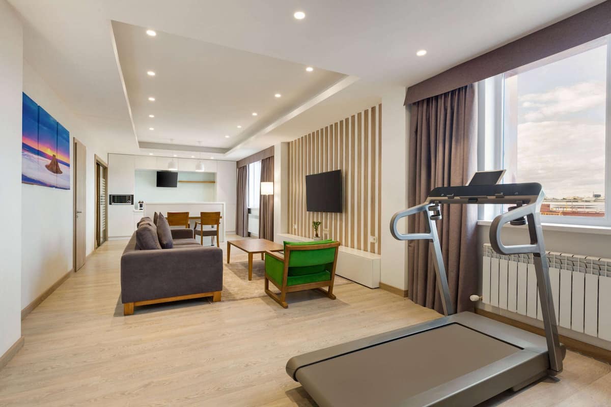 Habitación de hotel moderna con una cinta de correr, un sofá, una mesa de comedor y un televisor.