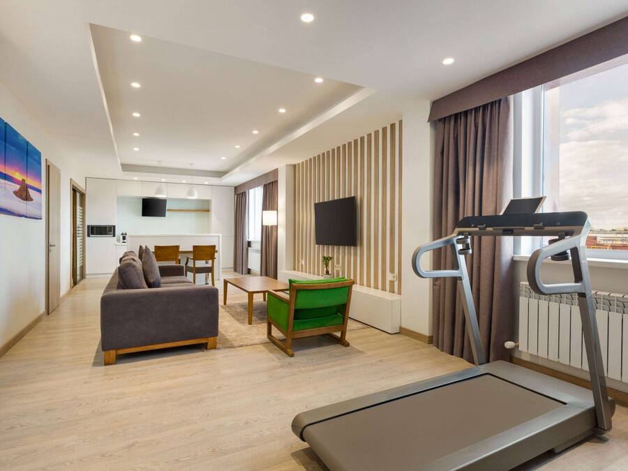 Ein modernes Hotelzimmer mit Laufband, einer Couch, einem Esstisch und einem Fernseher.