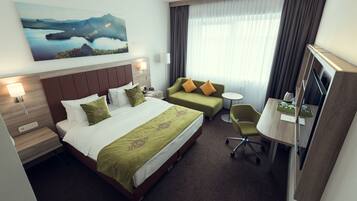 A hotel room with a large bed, a sofa, a desk with a chair, a TV, and a painting on the wall.