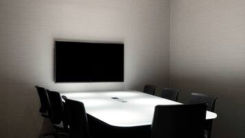 A conference room with a large flat-screen TV mounted on the wall, a white table, and black chairs.