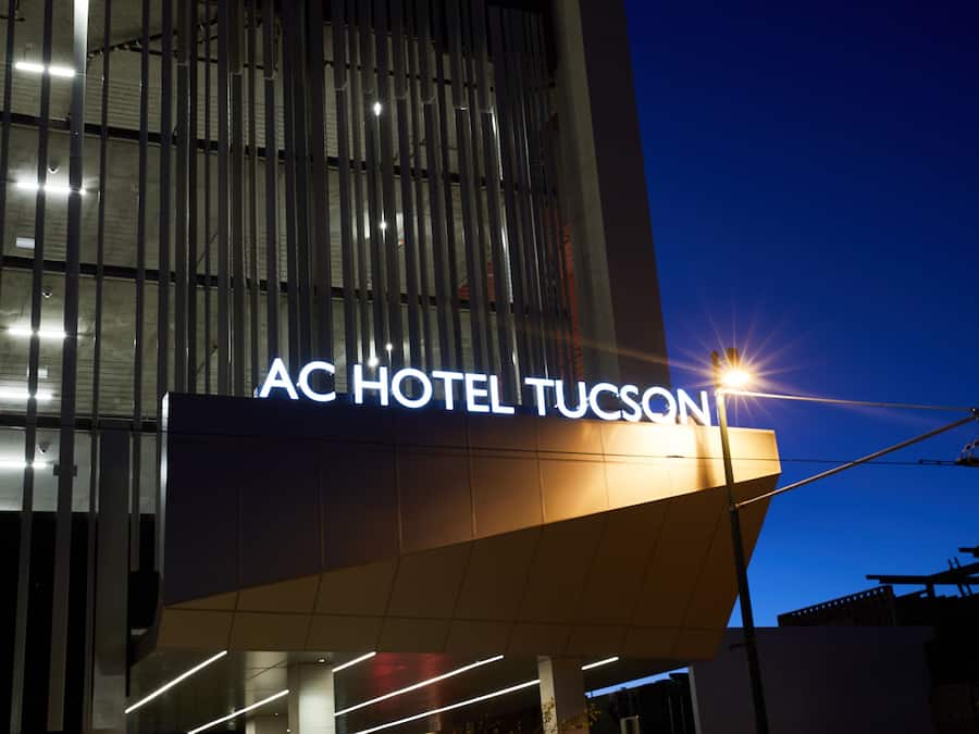 The exterior of the AC Hotel Tucson with a prominent illuminated sign.