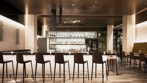 A bar area with multiple stools and a bar counter displaying various bottles. - AC Hotel by Marriott Tucson Downtown (Tucson)