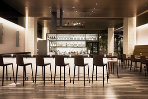 A bar area with multiple stools and a bar counter displaying various bottles. - AC Hotel by Marriott Tucson Downtown (Tucson)